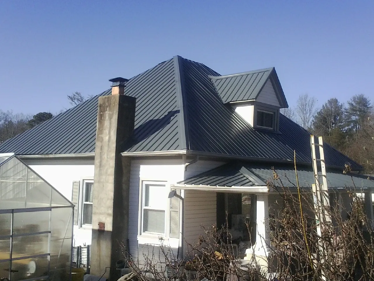 Dark blue standing seam metal roof on a white farmhouse with dormer — Slate & Tile Roof Repair by Roofing Brothers in Corinne