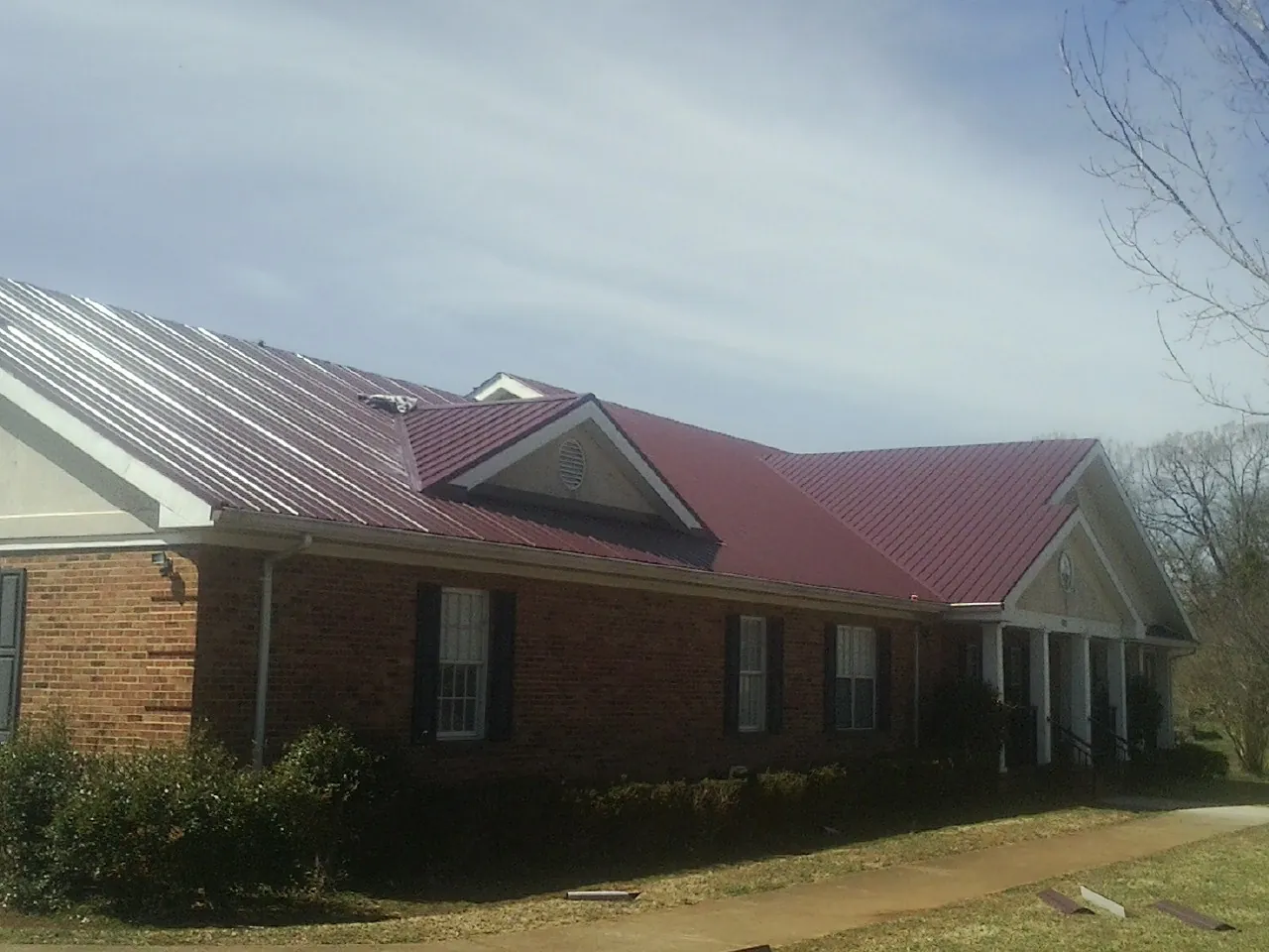 Red metal roof with gabled entries on a long brick building, from a Hail Damage Roof Repair job in Corinne