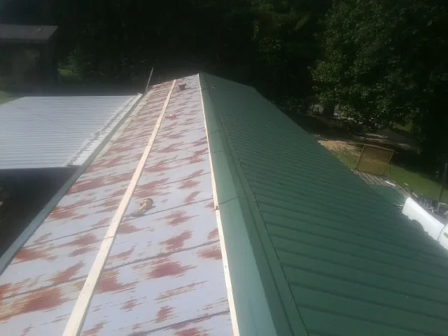 Old rusted panels beside newly installed green metal roofing — Wind Damage Roof Repair by Roofing Brothers in Corinne