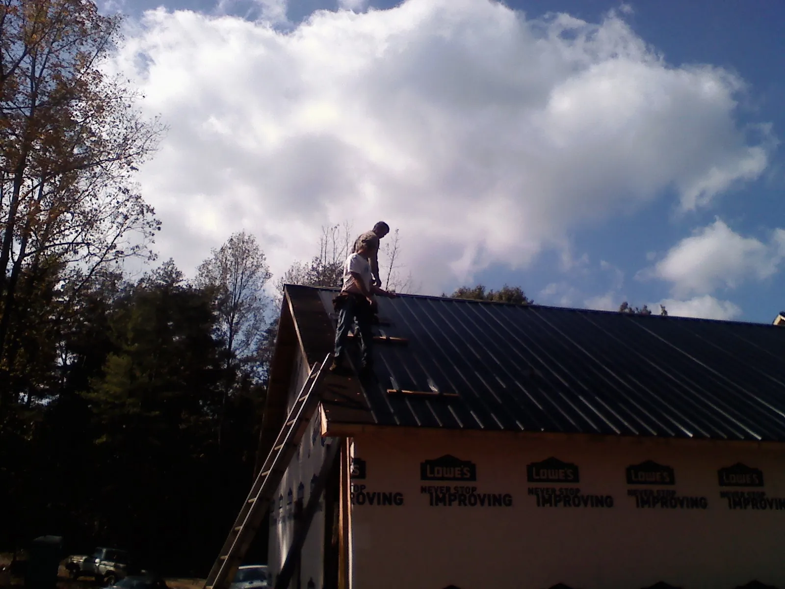 Roofer fastening dark metal panels high against a cloudy sky, from a Roof Inspection job in Corinne