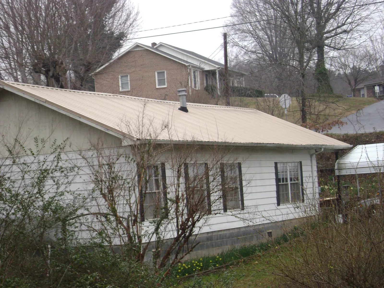 Tan metal roof on a white sided house set into a hillside — Commercial Roofing by Roofing Brothers in Corinne