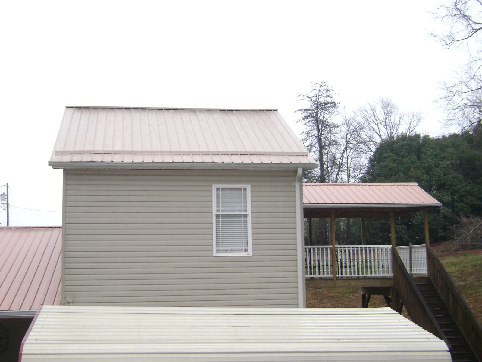 Tan metal roofs on a two story addition and attached porch, from a Roof Replacement job in Corinne